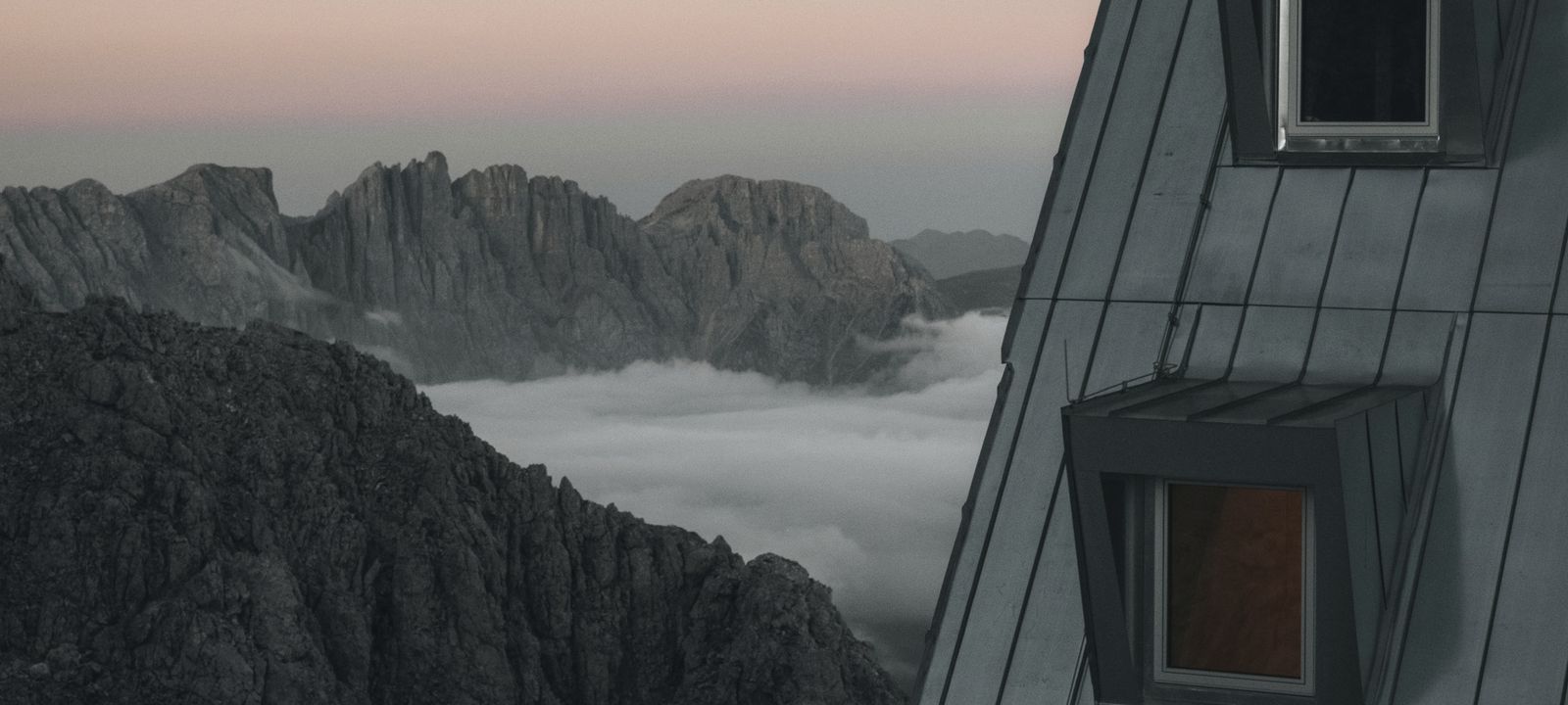Two windows of a metal-clad mountain hut looking out over a sea of cloud