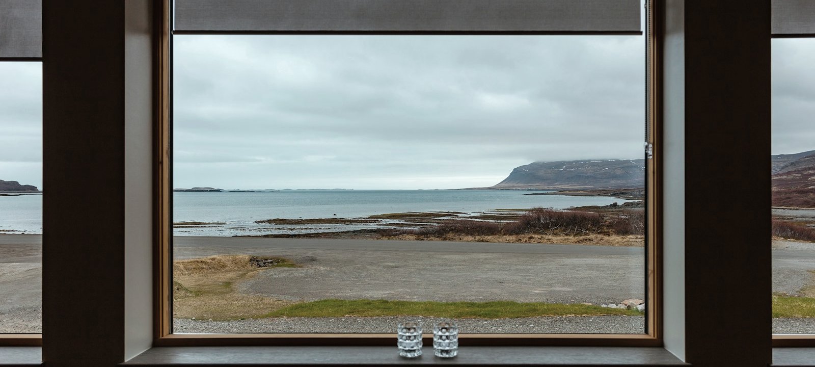 A table set with two glasses by a wide window onto a grey coast